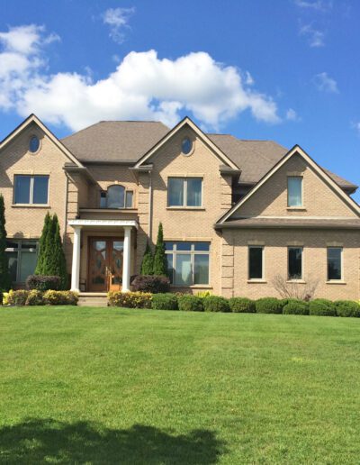 Large two-story brick house with a green lawn under a clear blue sky.