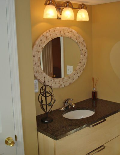 A small bathroom with a round mirror, single sink vanity, and tan walls.
