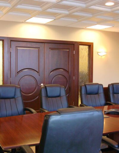 Conference room with a large wooden table, leather chairs, and double doors.