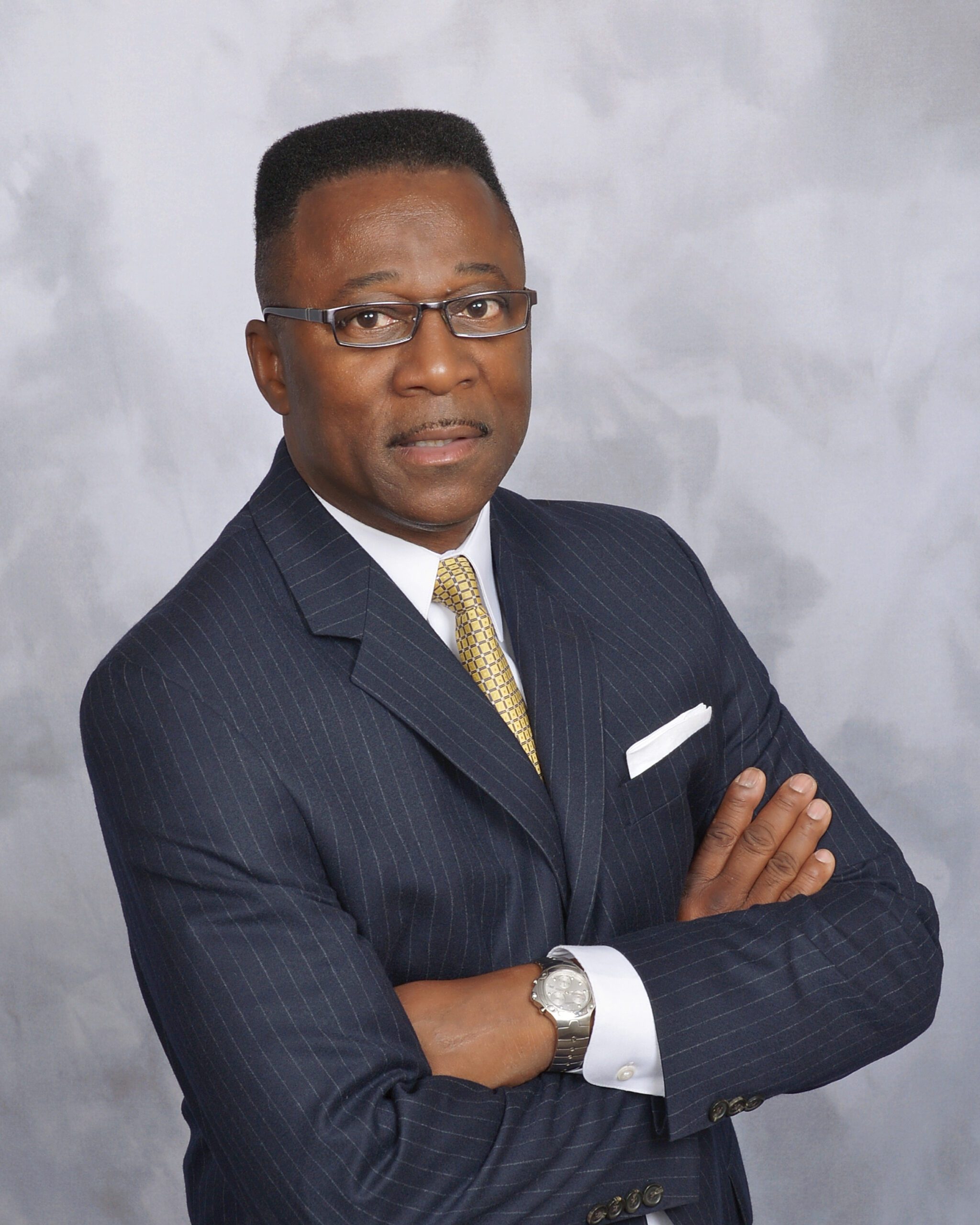A professional man in a pinstriped suit with folded arms against a grey backdrop.