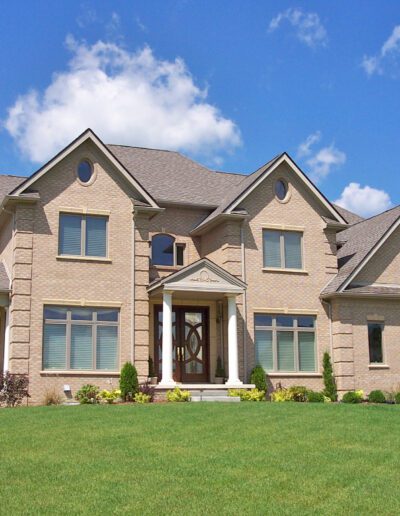 A spacious two-story suburban home with a well-manicured lawn under a clear blue sky.