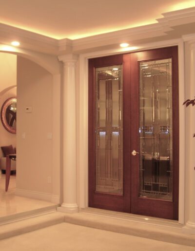 An elegant interior with a wooden double door featuring glass panels, surrounded by decorative columns.