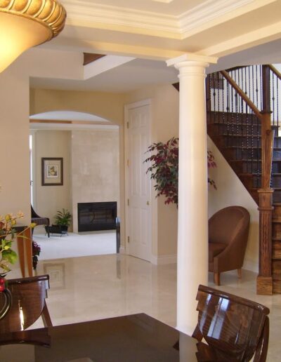 Elegant interior of a house featuring glossy tiled floors, a wooden staircase, and decorative columns.
