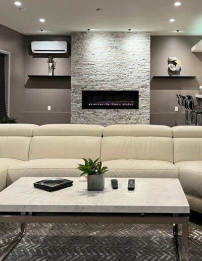 Modern living room with large white sectional sofa, a marble coffee table, and an electric fireplace set in a stone wall.