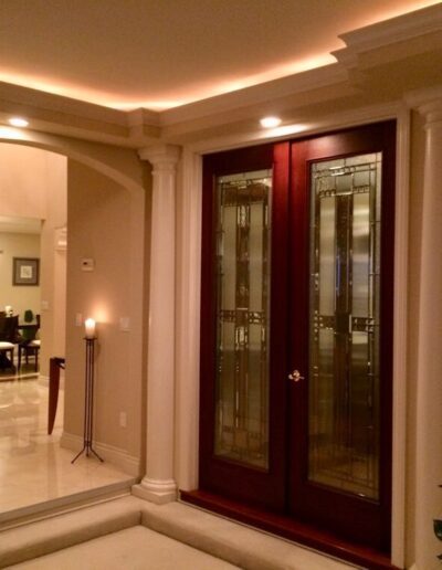 An elegant interior with polished floors, flanked by classical columns and illuminated by warm lighting, showcasing a wooden double door entrance to a dining area.