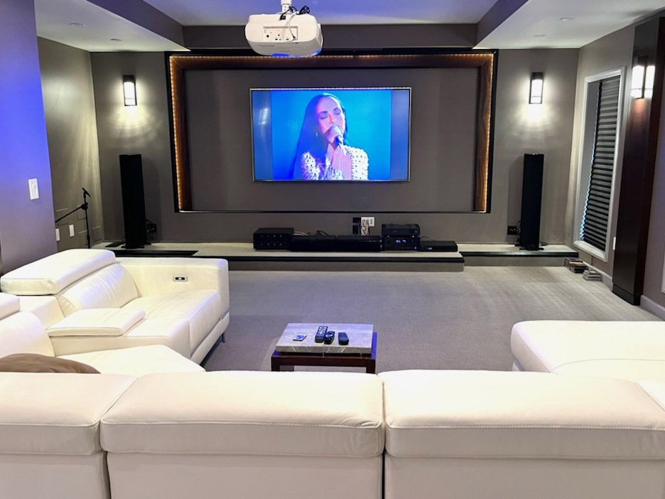 A modern home theater room with large screen and white sofas.