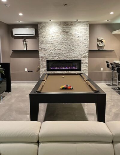 A modern entertainment room featuring a billiard table, sectional sofa, and a bar area in the background.